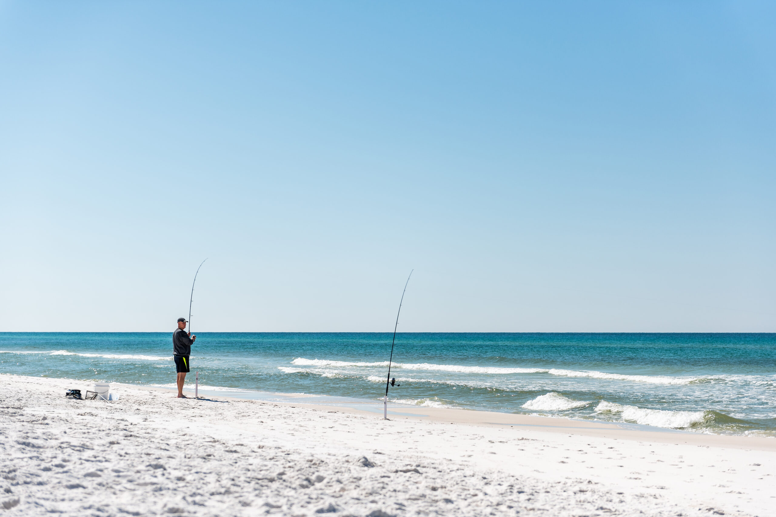 Un homme debout pêche avec tige sur la plage au cours de la journée ensoleillée dans le panhandle de Floride golfe du Mexique avec les vagues de l’océan, paysage, sable blanc